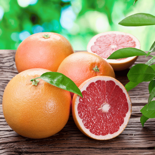 Three whole grapefruits and two halves are put on a wooden table outside