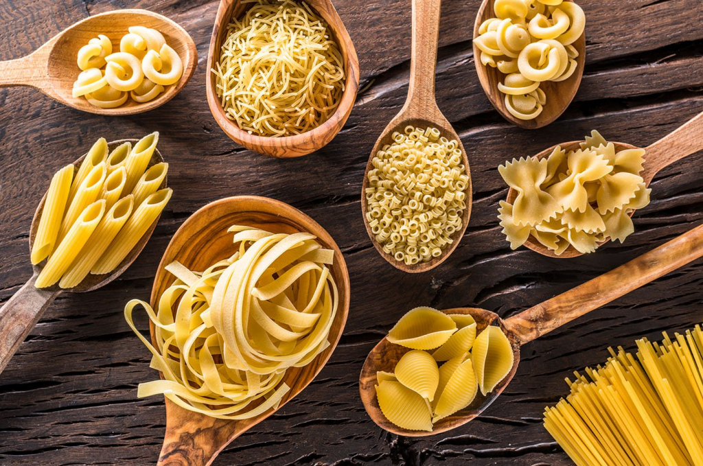 Nine different types of pasta in wooden spoons on a table